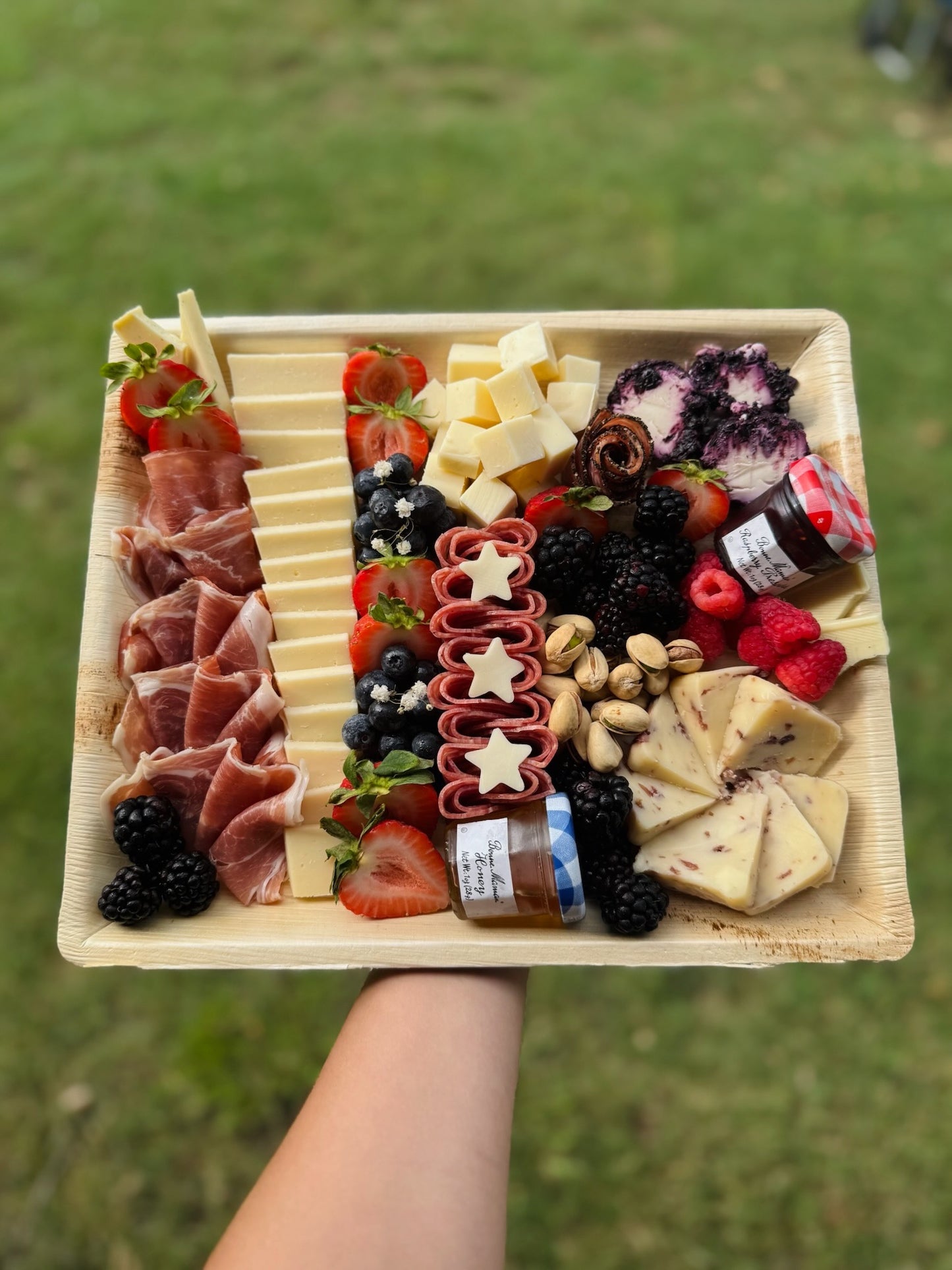 Assorted charcuterie board with meats, cheeses, fruits, and nuts on a wooden tray.