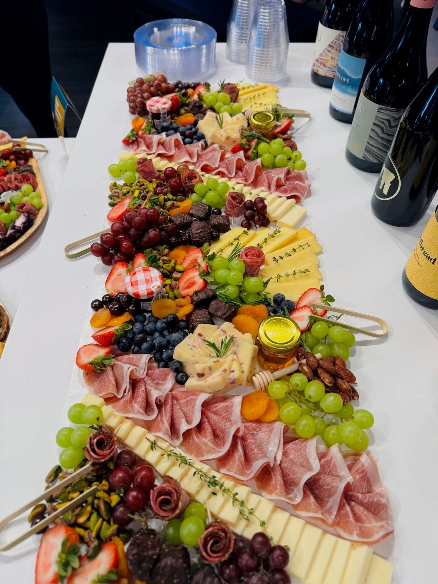 Diverse platter of meats, cheeses, fruits, and vegetables arranged in a decorative pattern on a white table.