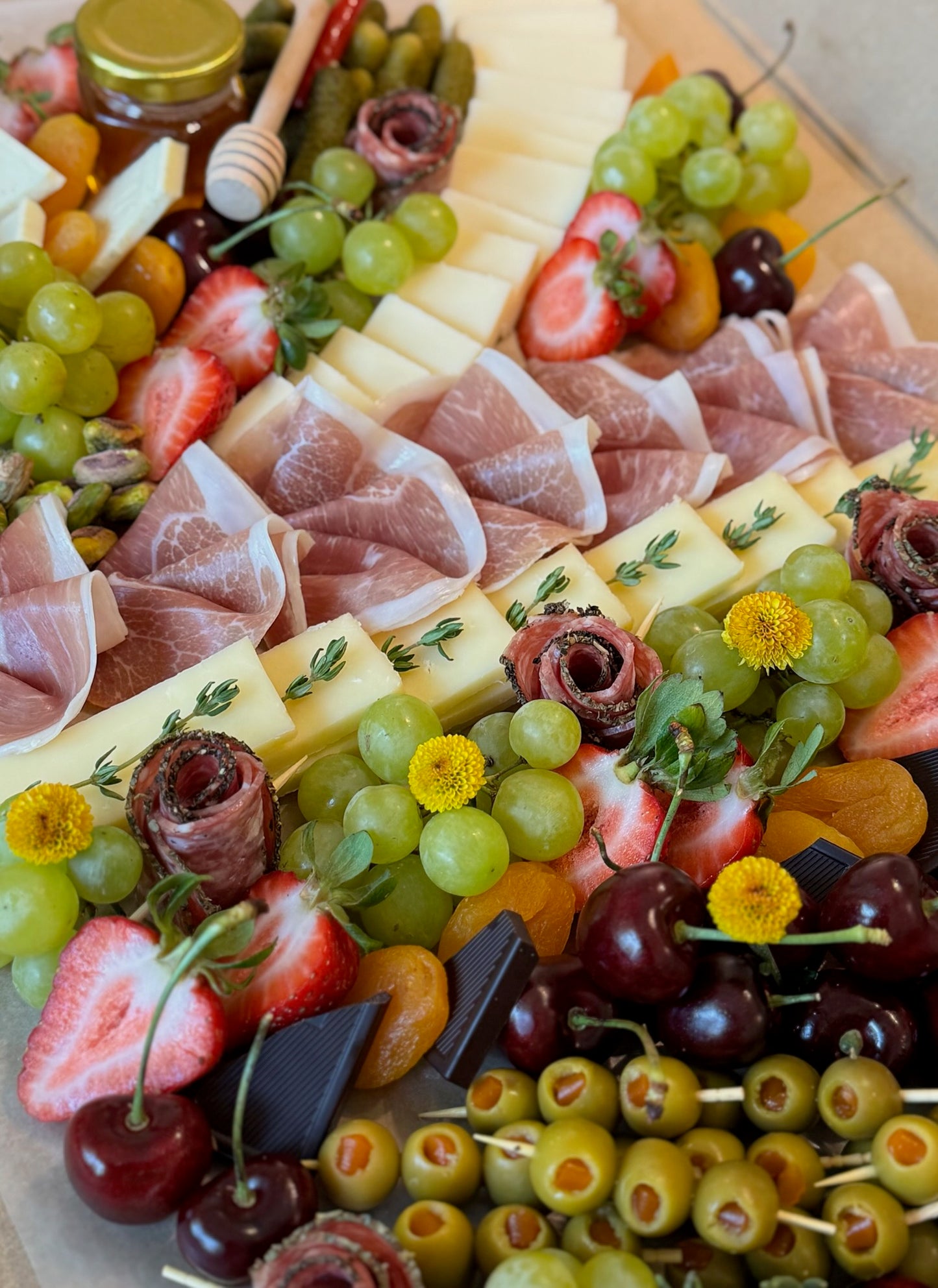 Assorted charcuterie board with meats, cheeses, fruits, and olives on a wooden board.