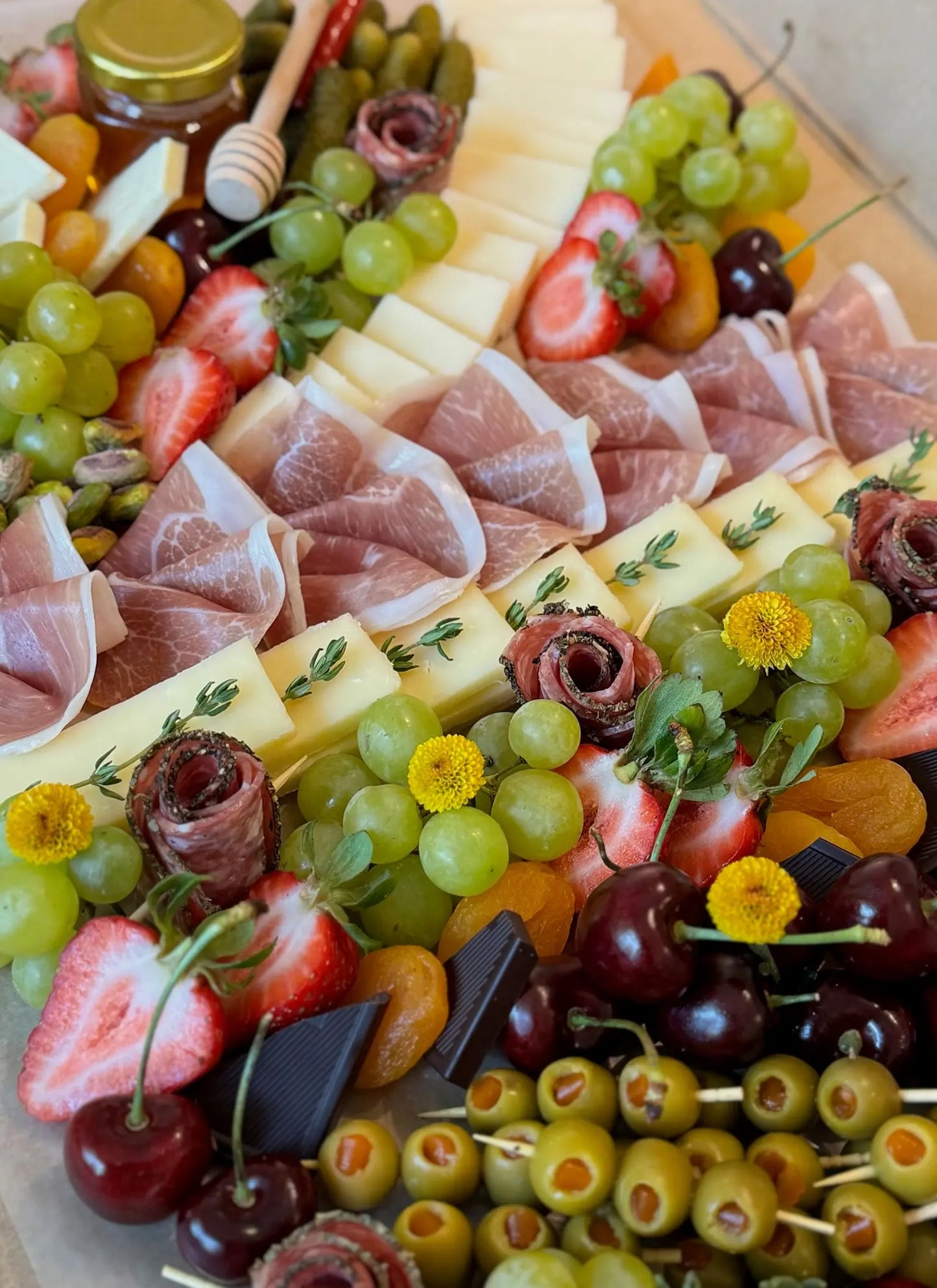 Assorted charcuterie board with meats, cheeses, fruits, and olives on a wooden board.