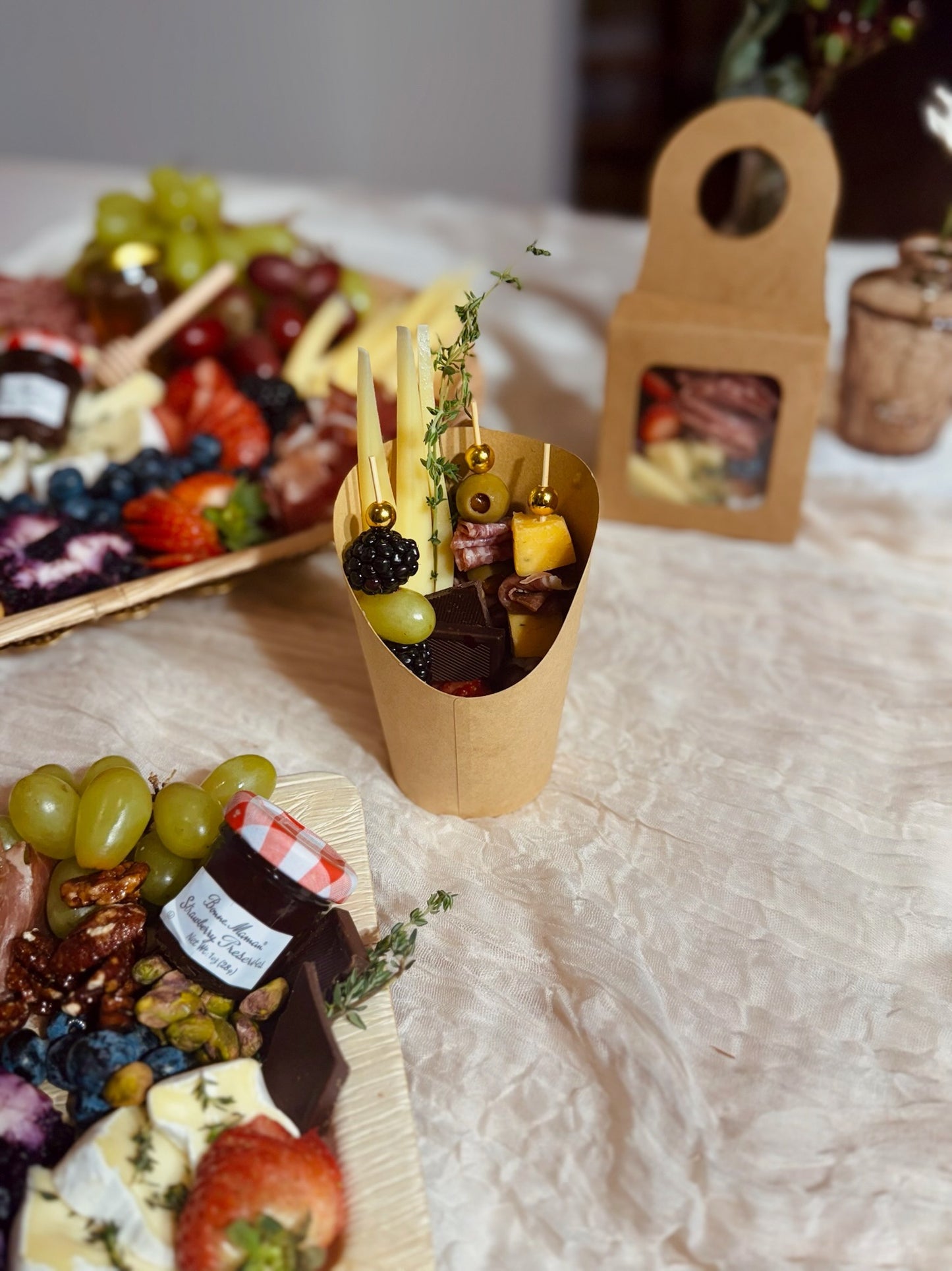 Assorted fruits and cheeses on a table with a small paper cone containing more fruits and in a personal sized cup