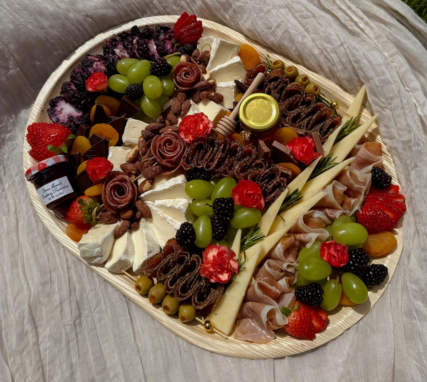 Decorative charcuterie board with meats, cheeses, fruits, and flowers on a wooden surface.