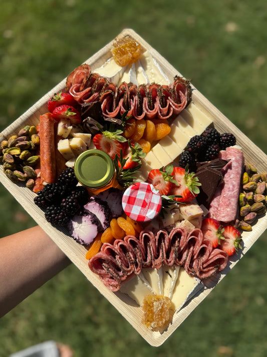 Platter of assorted meats, cheeses, and fruits on a wooden board held outdoors.