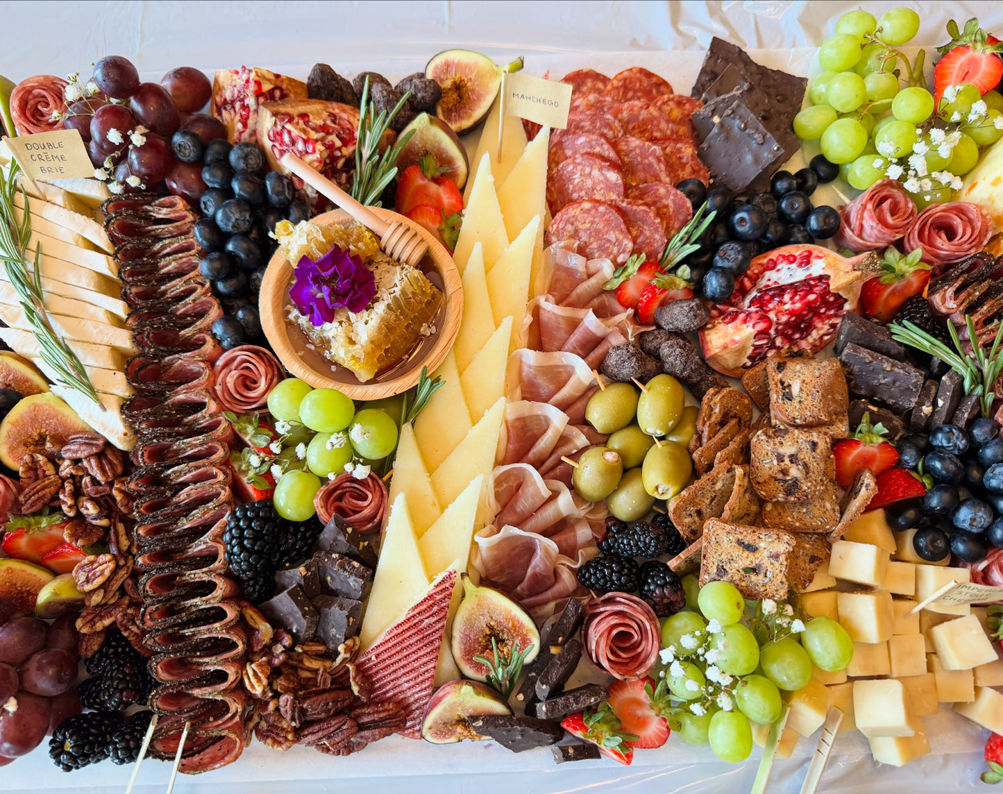 Assorted charcuterie board with meats, cheeses, fruits, and bread on a white surface.