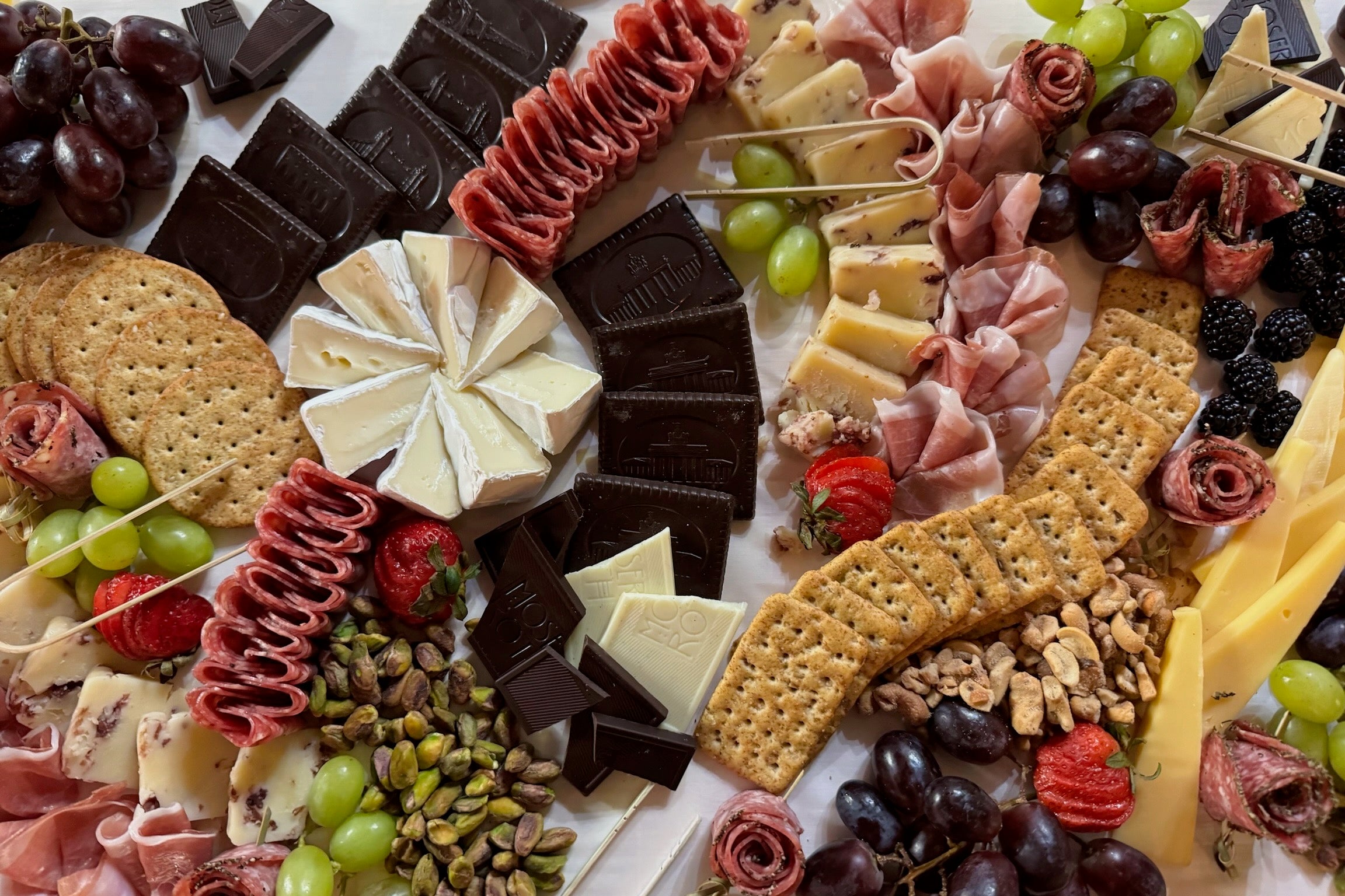 Assorted charcuterie board with meats, cheeses, crackers, and fruits on a white surface.