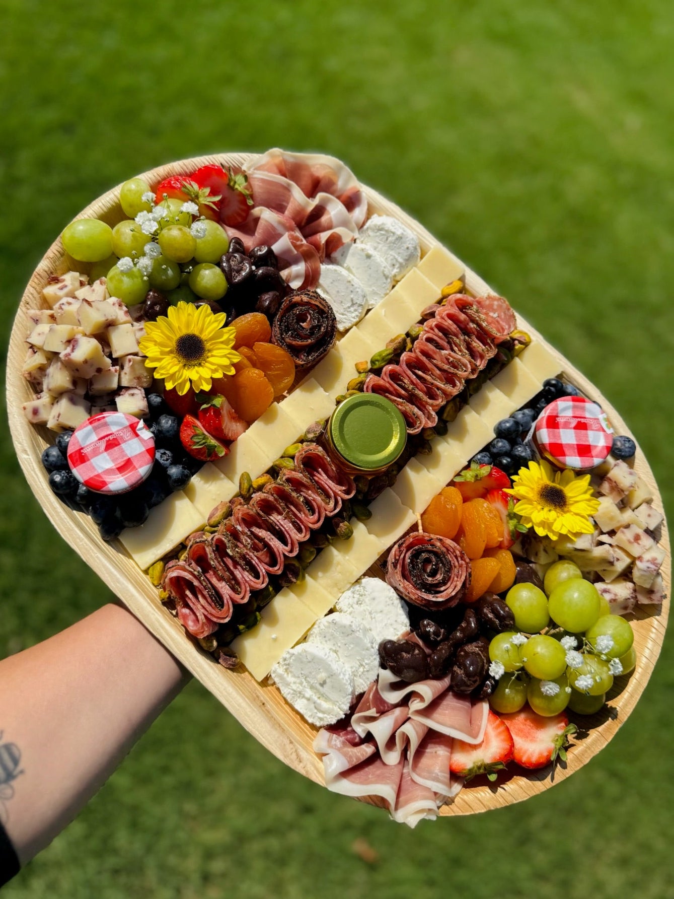 Platter of assorted meats, cheeses, and fruits held over a grassy background