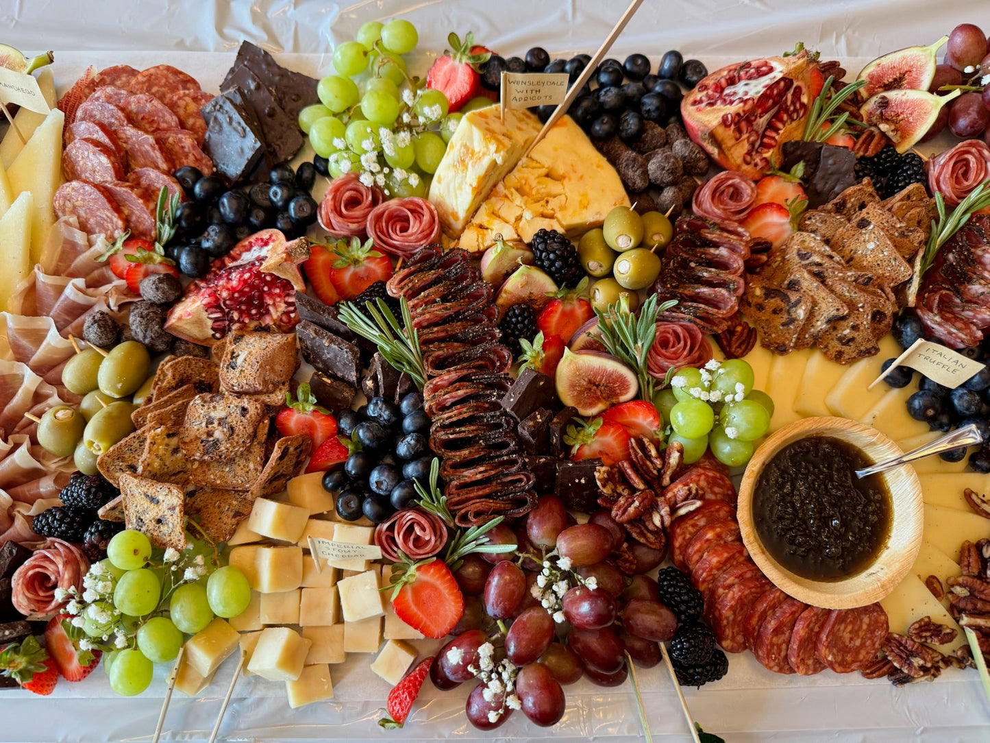 Assorted charcuterie board with meats, cheeses, fruits, and crackers on a white surface.