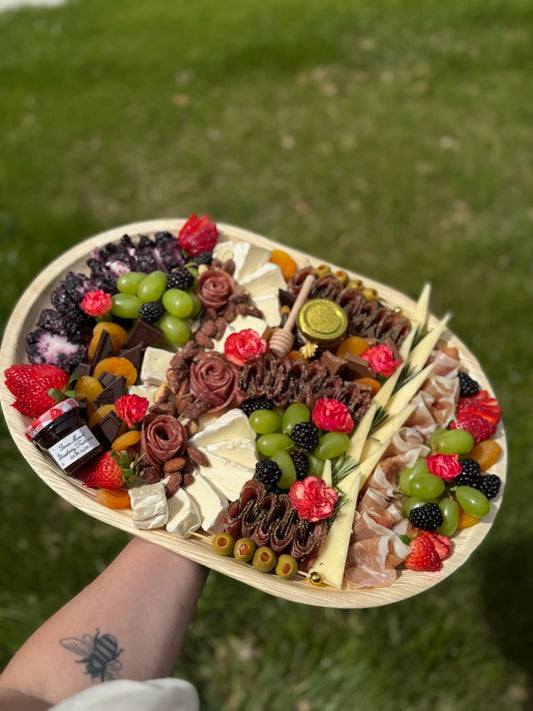 Platter of assorted fruits, cheeses, and meats held over a grassy background