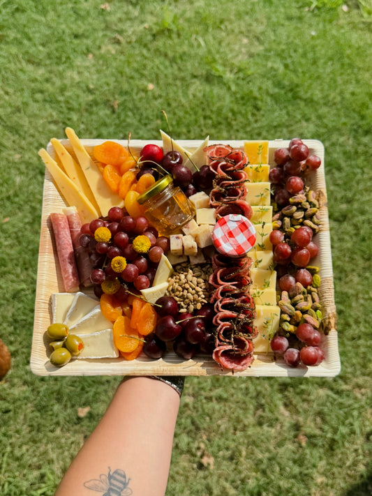 Assorted fruits, cheeses, and meats on a wooden board held over grass.